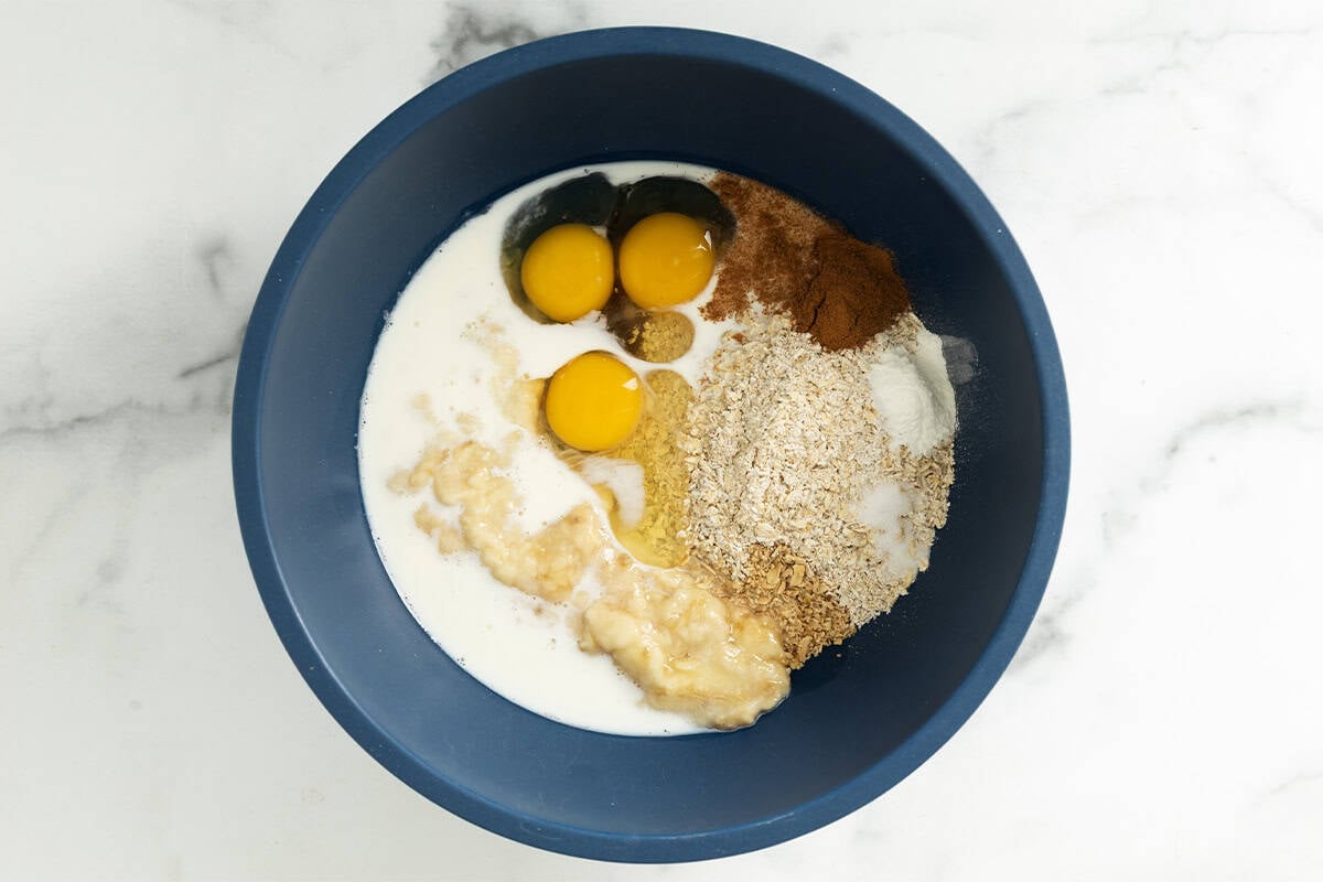 Ingredients for banana bread baked oatmeal in blue bowl before mixing.