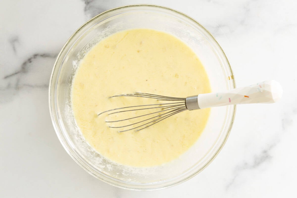 Wet ingredients for banana yogurt pancakes in glass bowl with whisk.