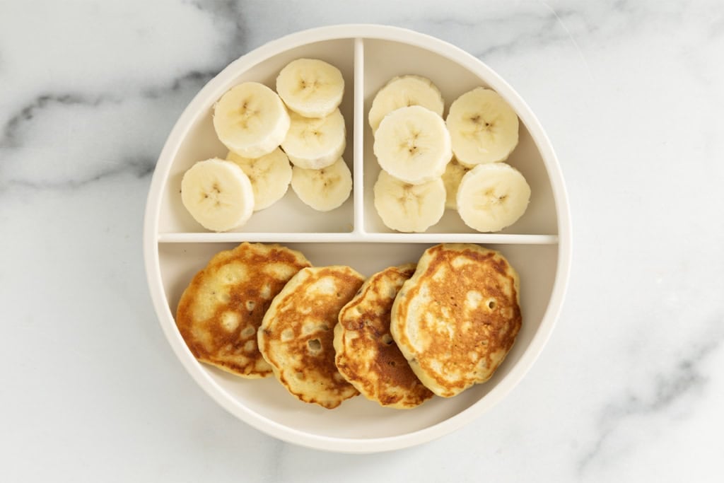Banana yogurt pancakes on kids plate with banana slices.