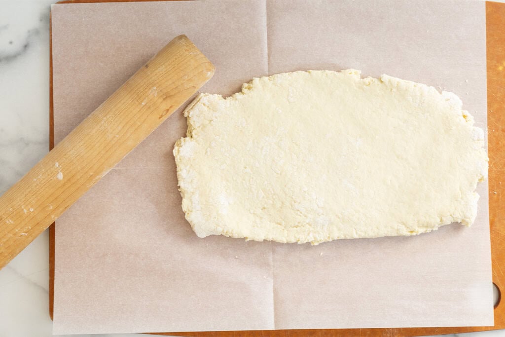 Dough for biscuits being rolled out on parchment paper.