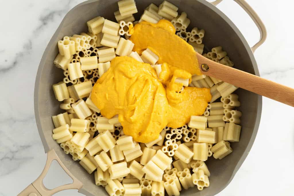 Carrot pasta sauce being added to noodles in pot.