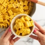 Hands holding bowl of carrot pasta over pot.