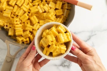 Hands holding bowl of carrot pasta over pot.