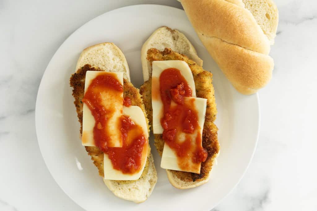 Assembling chicken cutlet sandwich on white plate.