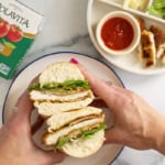 Hands holding chicken cutlet sandwich cut in half.
