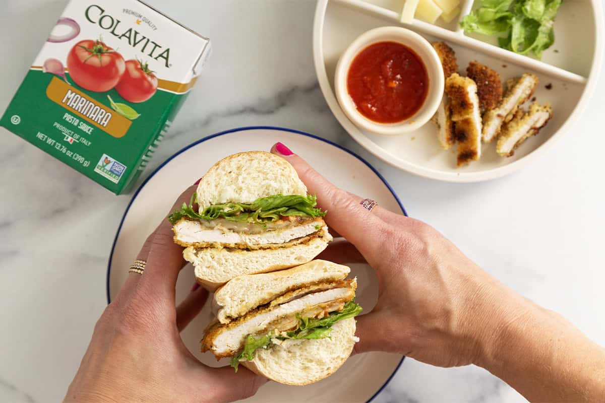 Hands holding chicken cutlet sandwich cut in half.