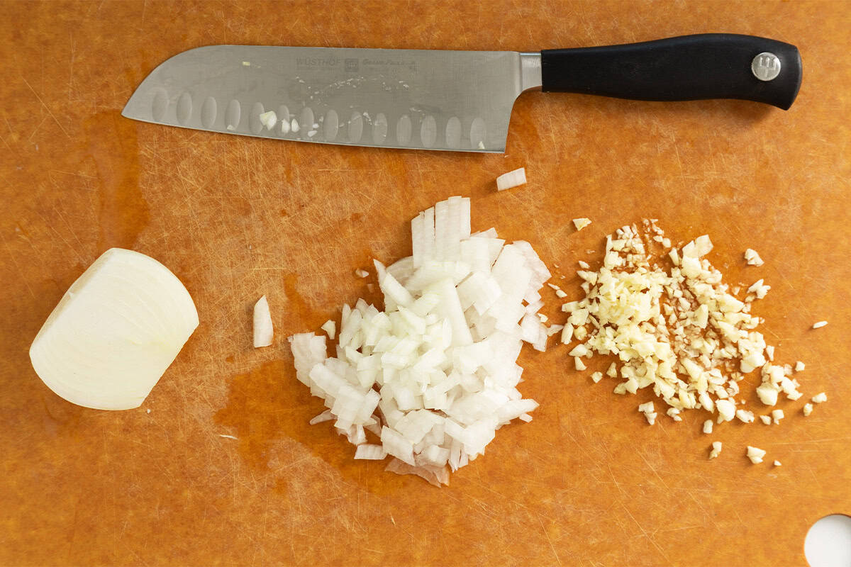 Onions and garlic chopped on cutting board for creamy pasta soup.