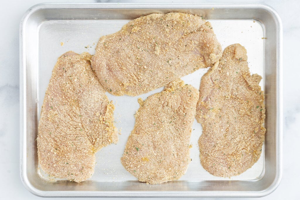 battered chicken cutlets on baking tray.