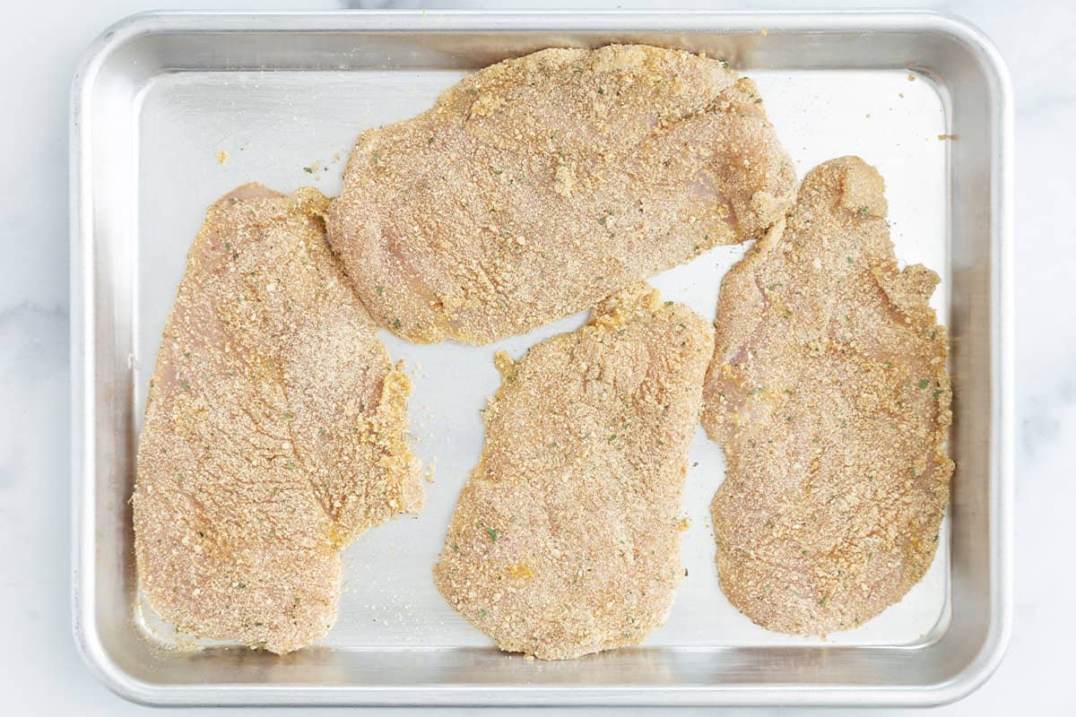battered chicken cutlets on baking tray.