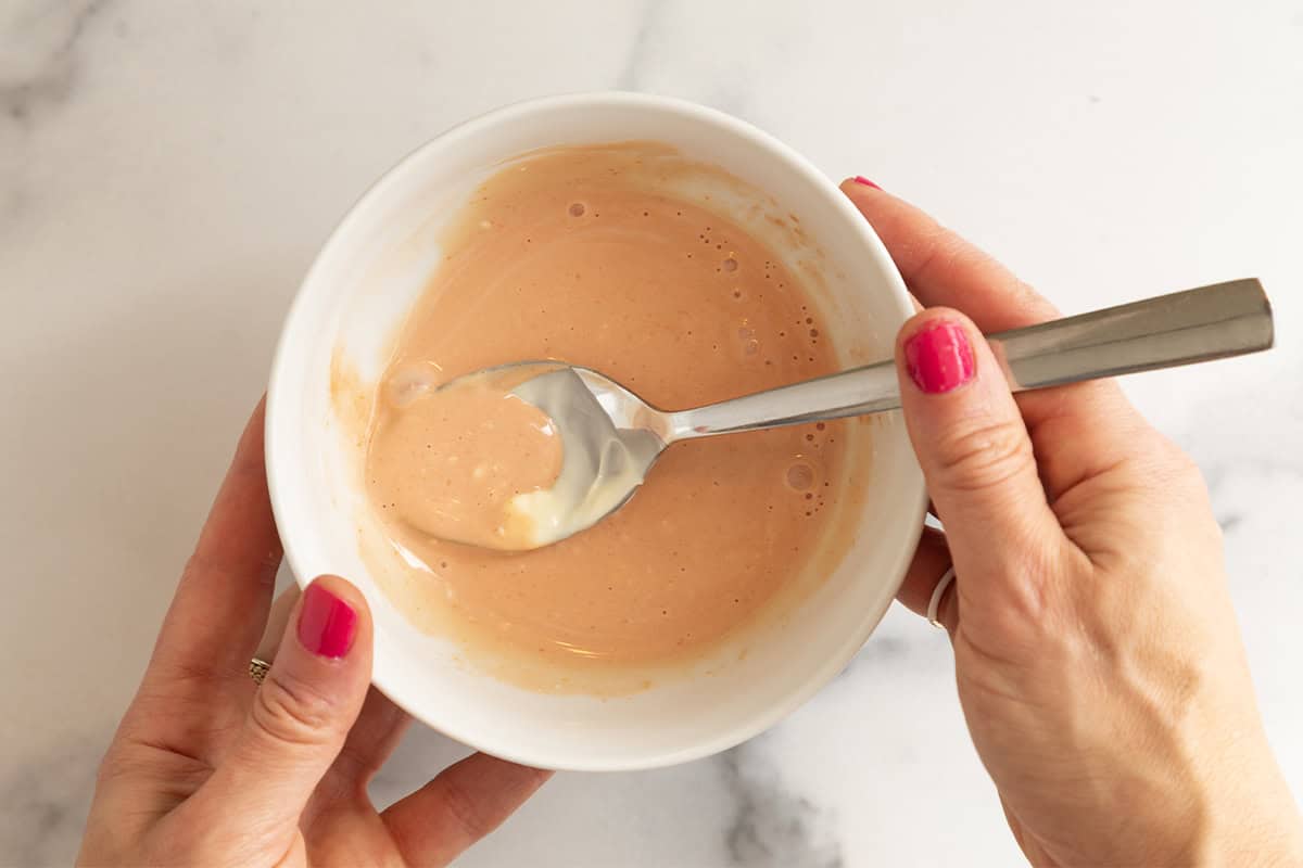 Dressing for cheeseburger salad in white bowl with spoon.