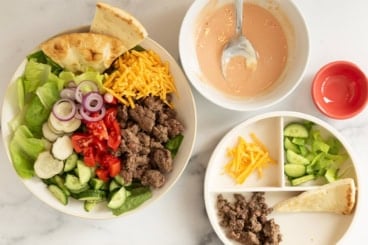 Cheeseburger salad with dressing on side on two plates.