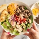 Hands holding white bowl of cheeseburger salad.