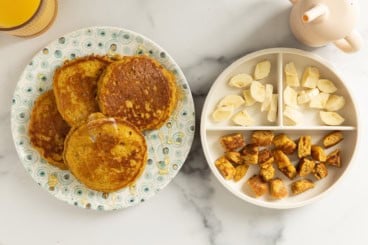 Pumpkin protein pancakes on two plates with bananas on side.