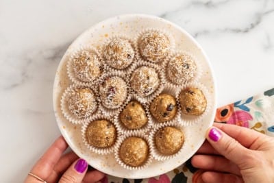 Almond butter protein balls on white plate with hands holding plate.