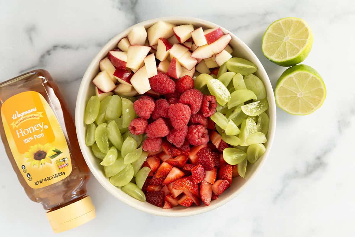 Christmas fruit salad in white bowl with lemon and honey on side.