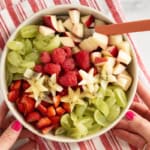 Hands holding Christmas fruit salad on stripped red towel with spoon.