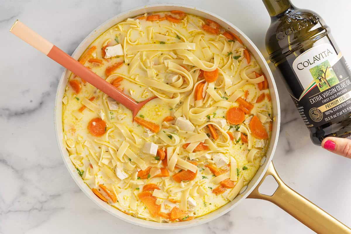 creamy chicken noodle soup in pot with olive oil bottle.