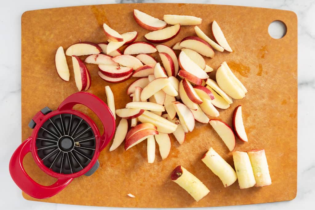 sliced apples with apple slicer on cutting board.