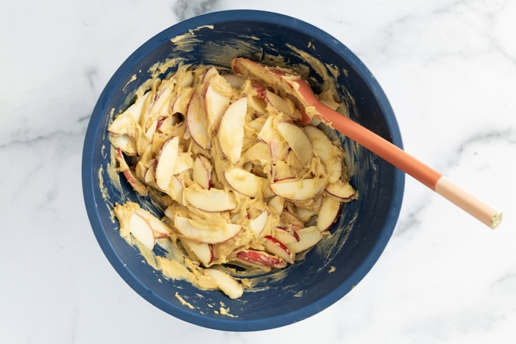 batter for apple cake with sliced apples in blue bowl.