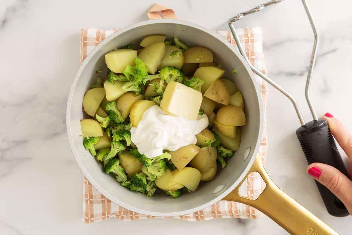 Sour cream and butter added to potatoes and broccoli in pot.