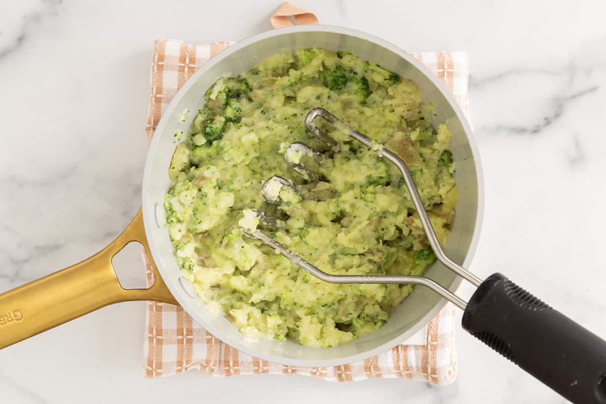Mashing potatoes and broccoli in pan.