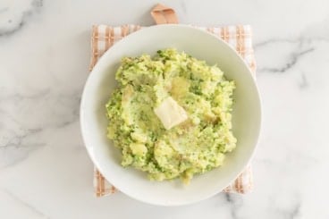 Mashed potatoes with broccoli on plate with butter.