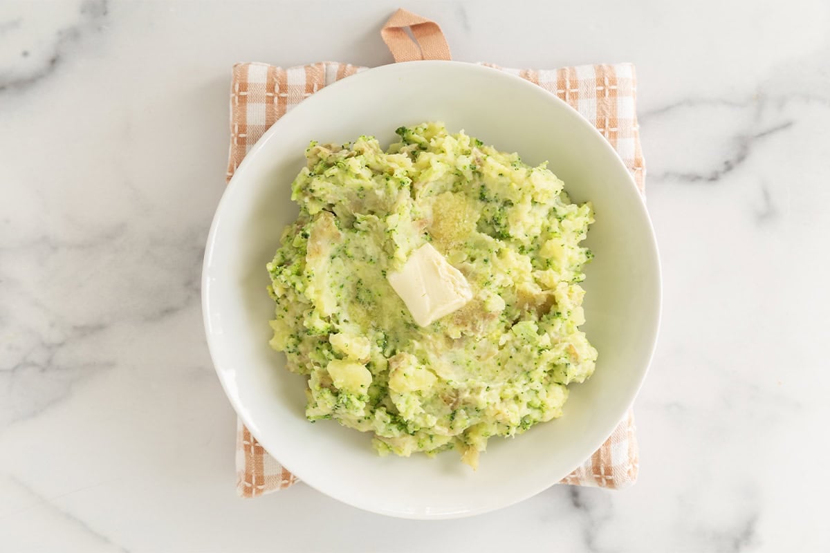 Mashed potatoes with broccoli on plate with butter.