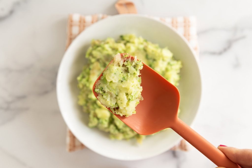 Spatula scooping mashed potatoes with broccoli.