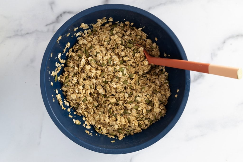 Olive oil granola mixture in blue bowl with spoon.