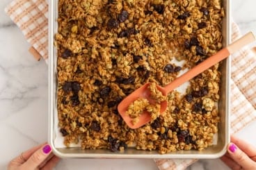 Olive oil granola on baking sheet with spatula.