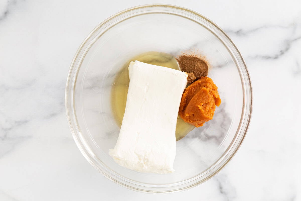 Ingredients for pumpkin cheesecake bites in glass bowl before mixing.