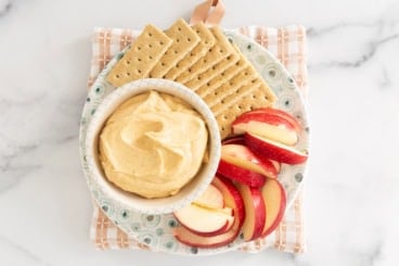 Pumpkin cheesecake dip in bowl with apples and crackers on side.