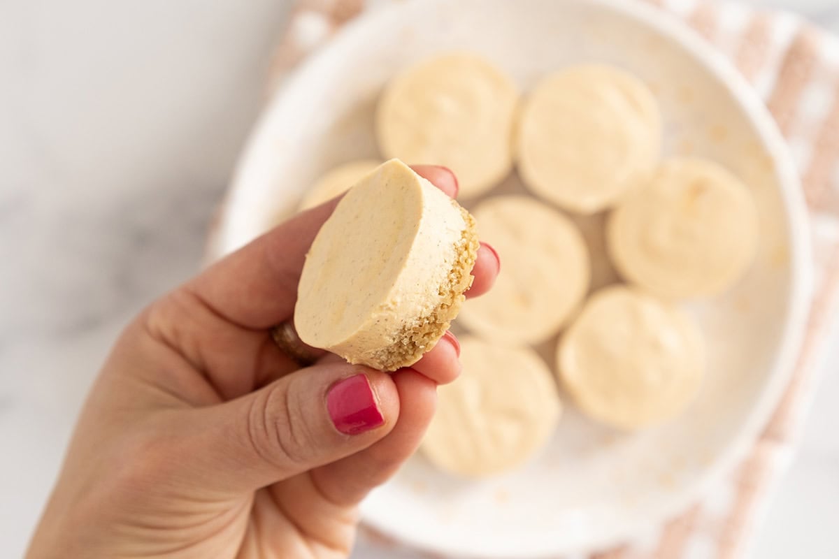 Hands holding pumpkin cheesecake bite.
