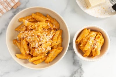 Roasted vegetable pasta in two bowls with cheese on top.