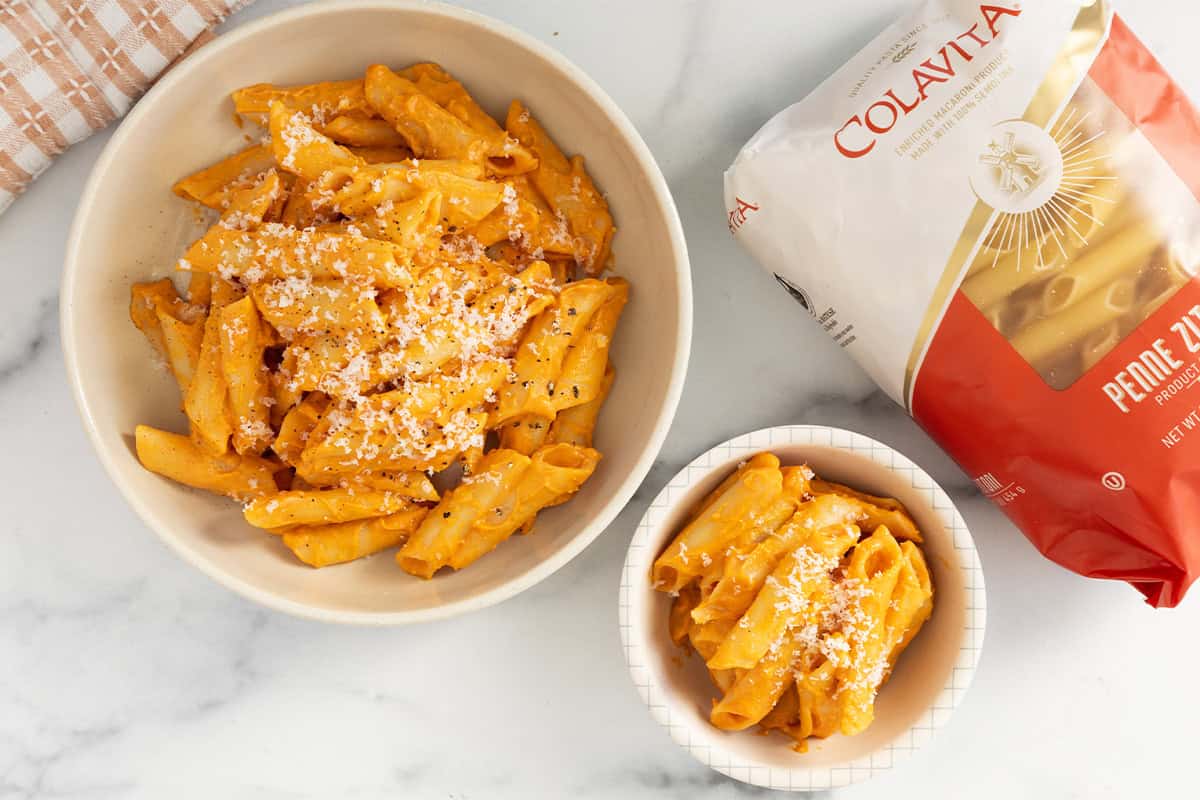 Roasted vegetable pasta in two bowls with cheese on top.