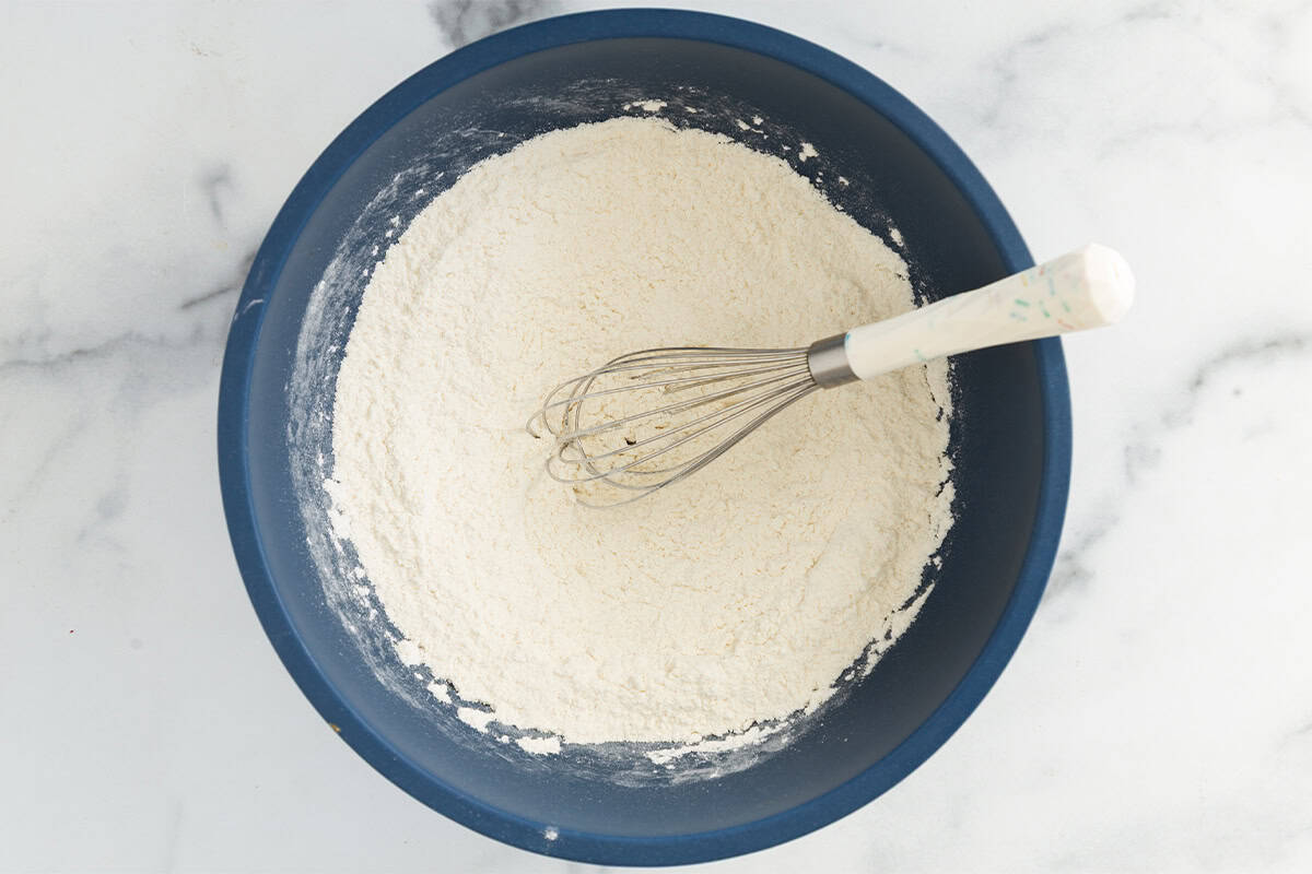 Dry ingredients for yogurt cupcakes in blue bowl with whisk.