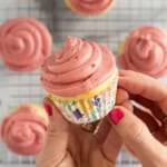 Hands holding yogurt cupcake with pink frosting.