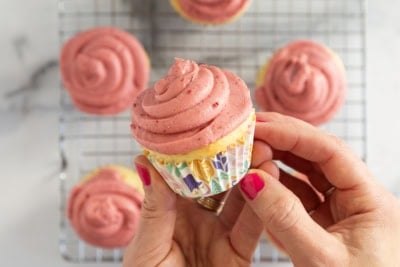 Hands holding yogurt cupcake with pink frosting.
