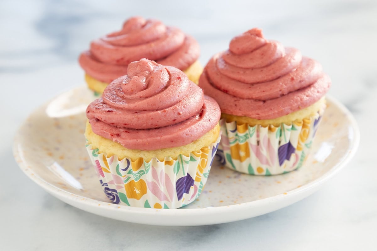 Three yogurt cupcakes on white plate with pink frosting.