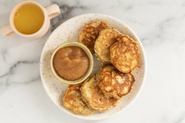 Apple oatmeal pancakes on white plate with applesauce.