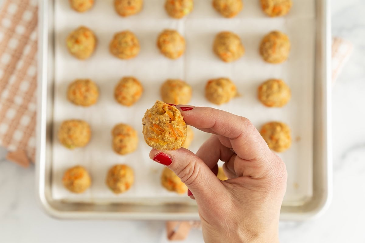 Asian chicken meatballs on baking sheet with hands holding one.