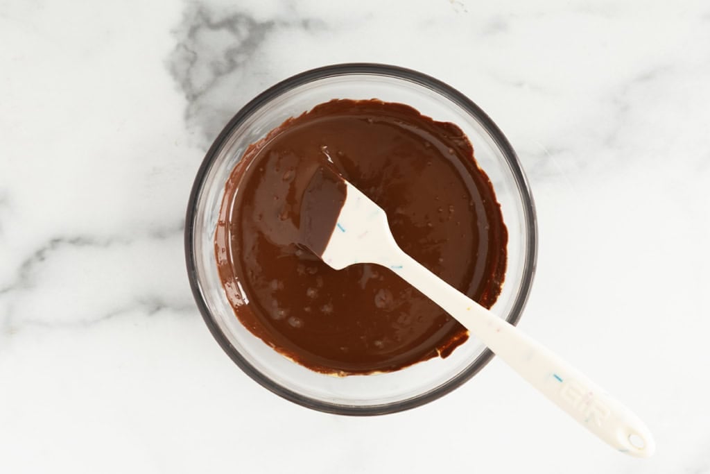 Melted chocolate and peanut butter in glass bowl with spatula.