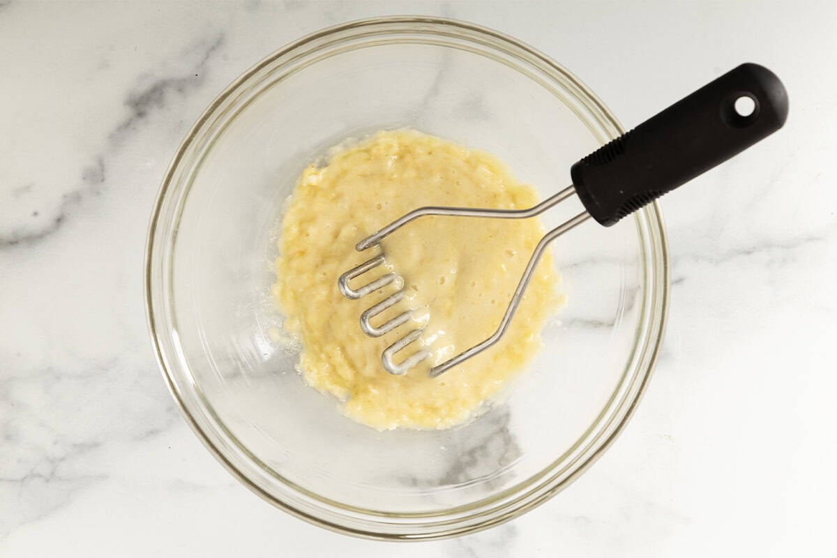 Banana being mashed in glass bowl.