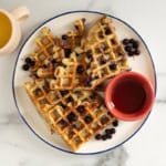 Blueberry waffles on plate with syrup and blueberries.