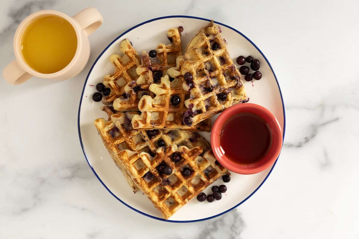 Blueberry waffles on plate with syrup and blueberries. 