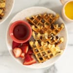 Chocolate chip waffles on white plate with syrup and strawberries.