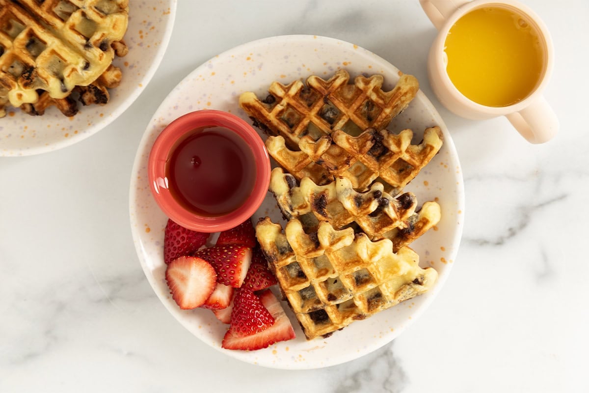 Chocolate chip waffles on white plate with syrup and strawberries.