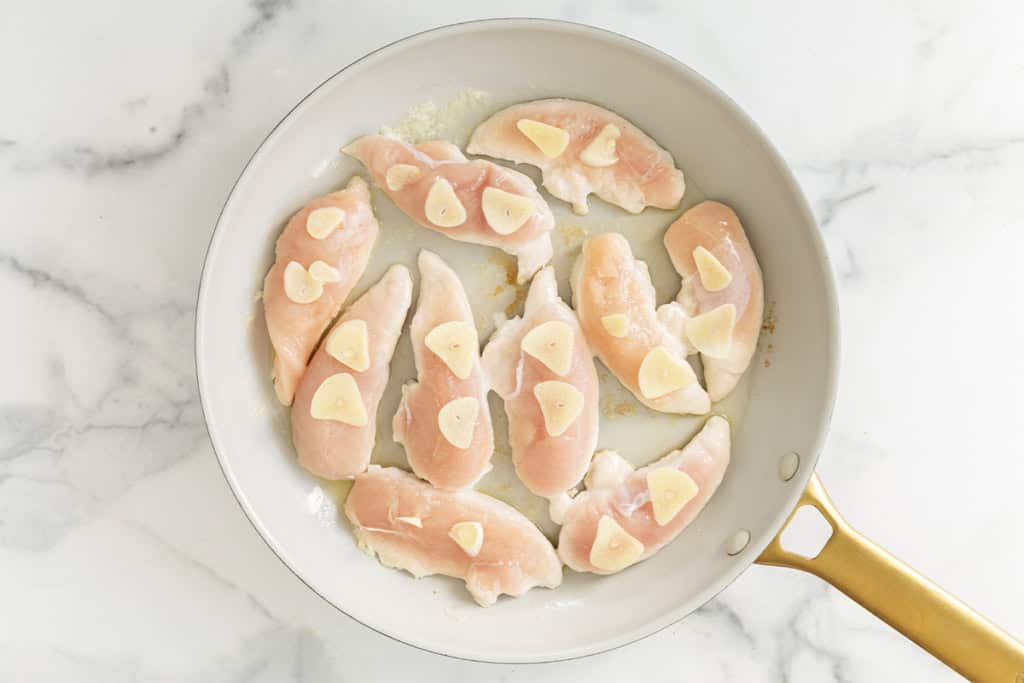 Chicken and garlic in frying pan for pan seared chicken.