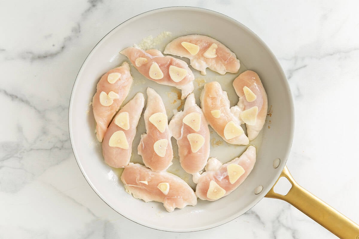 Chicken and garlic in frying pan for pan seared chicken.