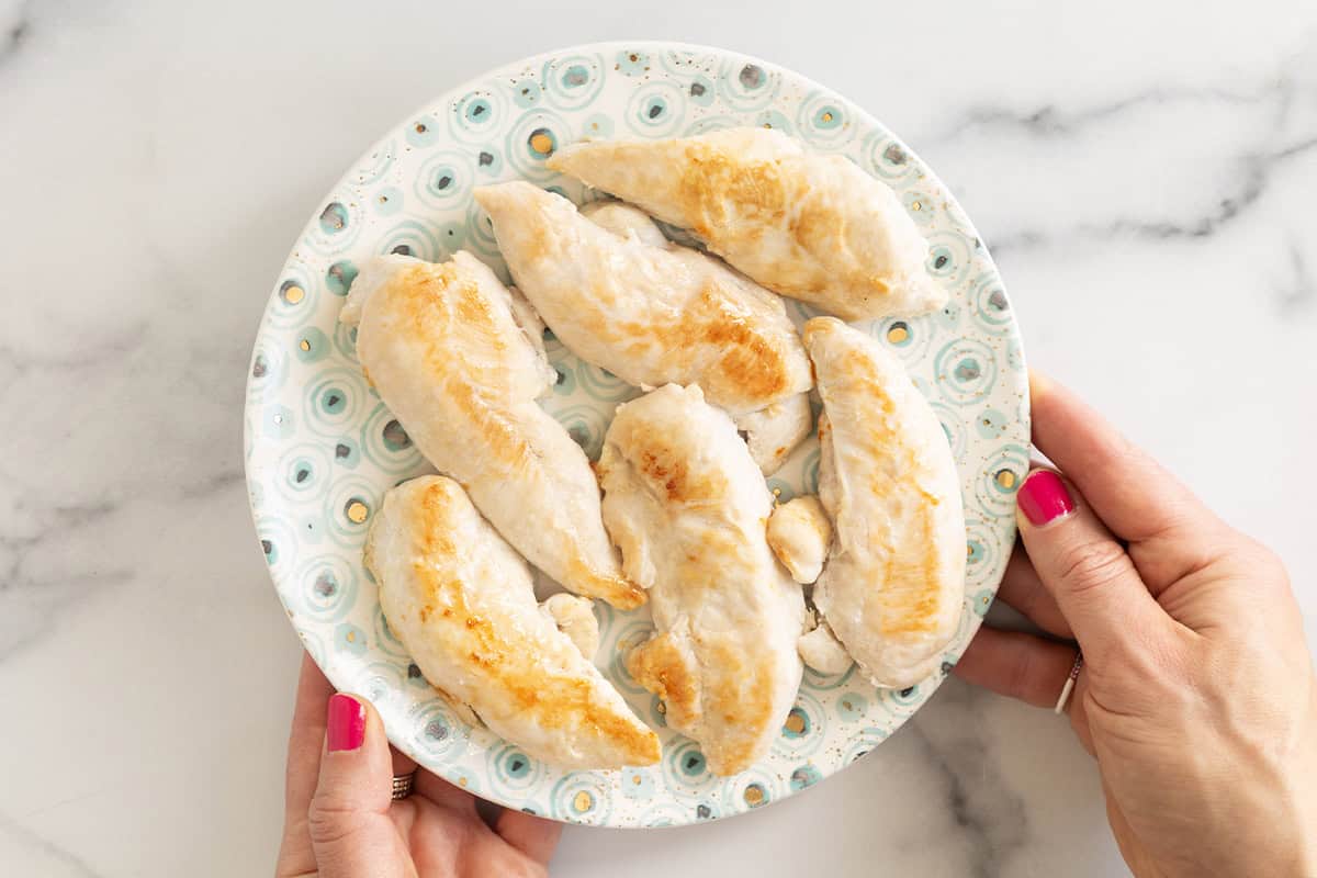 Pan seared chicken on plate with hands holding plate.